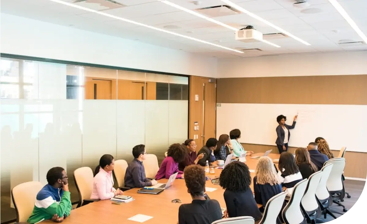 A diverse group of individuals attentively listens to a presenter in a modern conference room with a whiteboard.